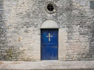 Il portale lunato d�ingresso, che include una porta blu in ferro con croce dorata, � sormontato da un oculo in asse